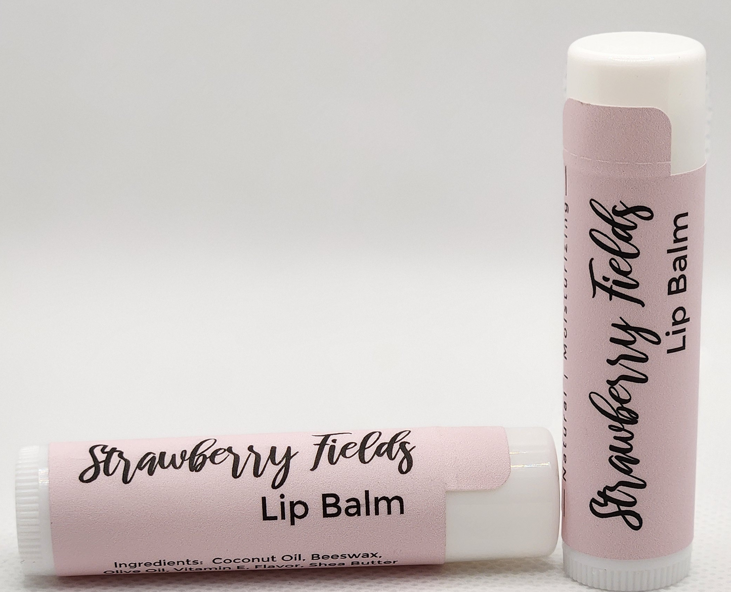 A sleek, eco-friendly tube of Strawberry Fields lip balm, with a minimalist design and clear labeling. The tube is a light, natural color with the product name displayed in elegant, clean fonts.