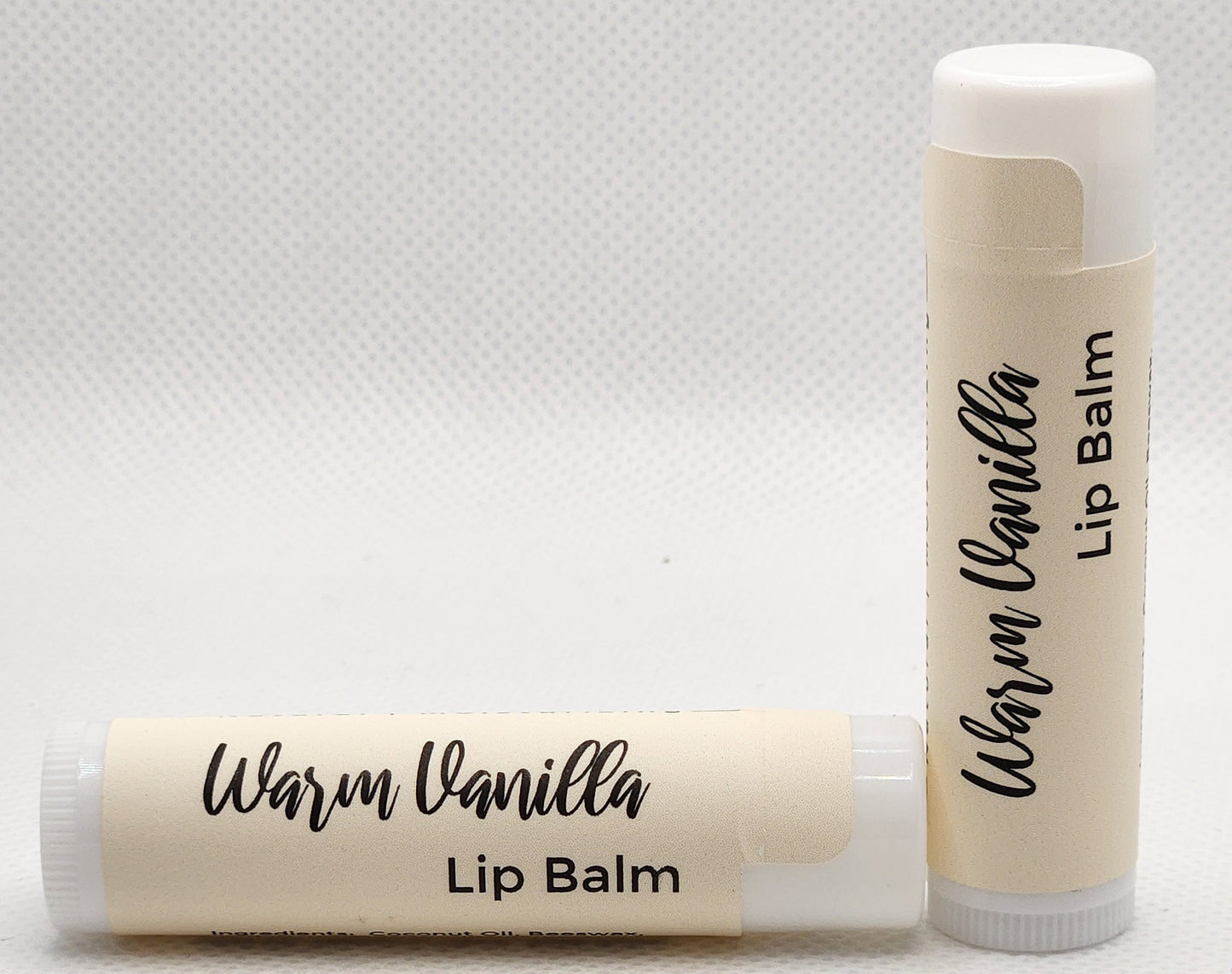 A sleek, eco-friendly tube of warm vanilla lip balm, with a minimalist design and clear labeling. The tube is a light, natural color with the product name displayed in elegant, clean fonts.