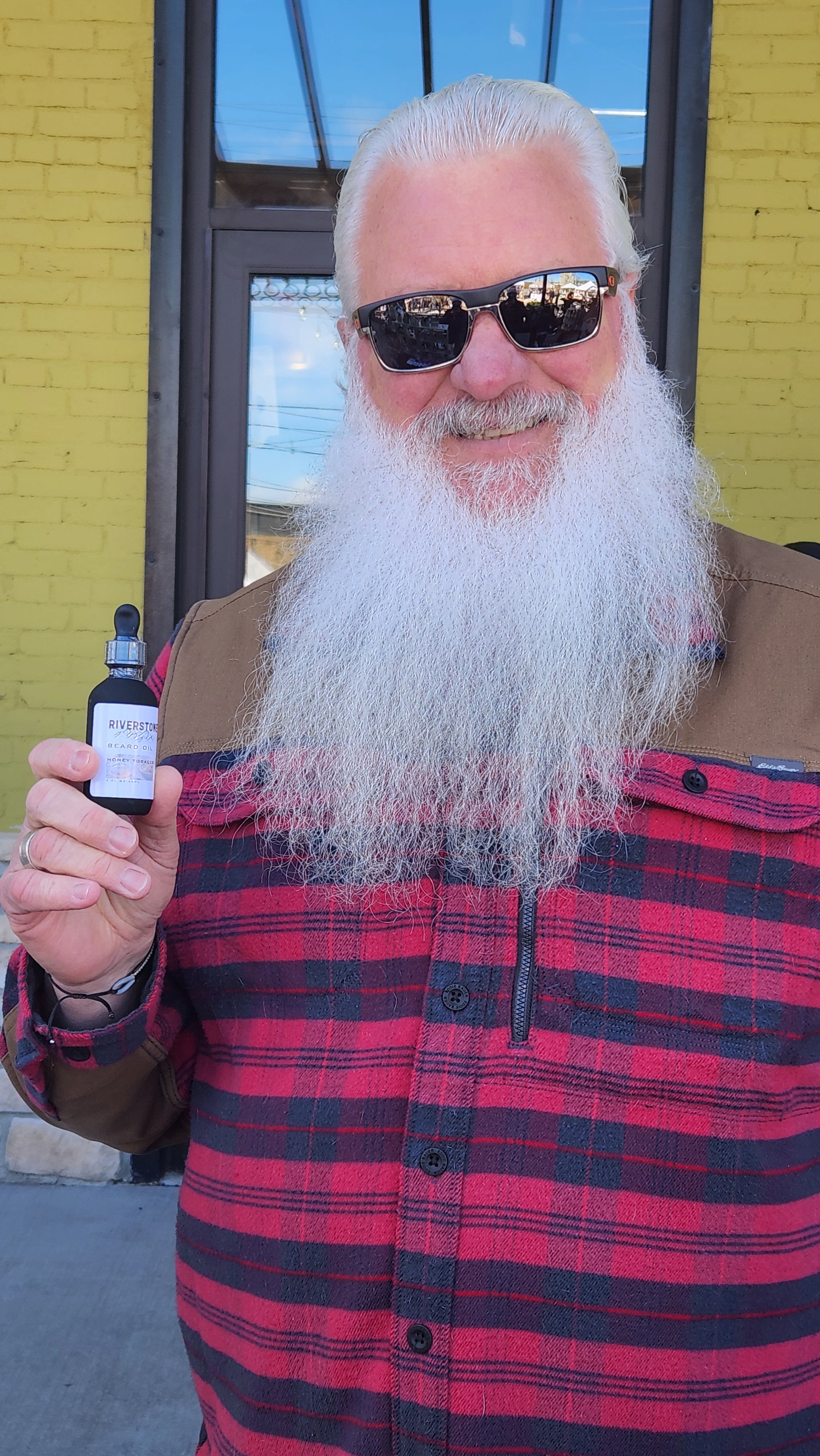 Real customer who has a long white beard who is holding Riverstone Beard Oil bottle